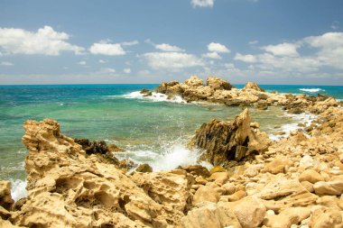 Turkuvaz suları, kumlu bir plaj, kayalık kıyı şeridi ve açık mavi gökyüzü içeren nefes kesici Kıbrıs Akdeniz manzarası. Yaz tatilleri, turizm ve doğa aşıkları için mükemmel bir tatil yeri..