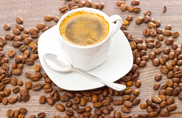 Šálek kávy a kávových zrn na dřevěném stole — Stock fotografie