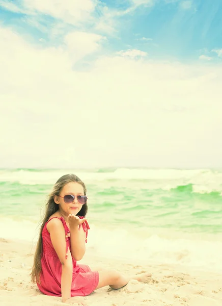 Little girl in sunglasses sending a kiss while sitting at the se — Stock Photo, Image