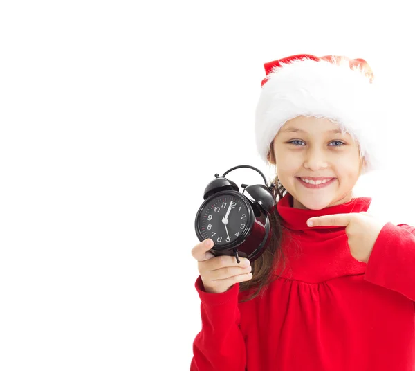 Little girl in Santa Claus hat holding alarm clock and points a — Stock Photo, Image