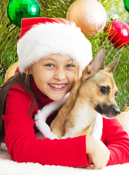 Flicka i en röd jul klä kramas hund på bakgrund av t — Stockfoto
