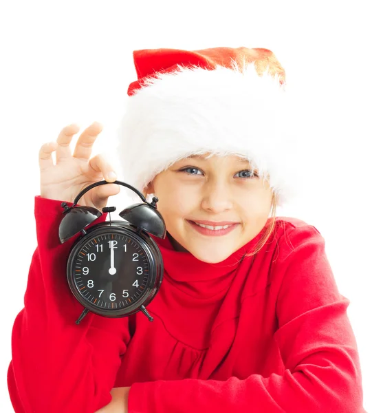 Niña en el sombrero de Santa Claus sosteniendo reloj despertador que muestra doce —  Fotos de Stock