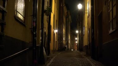 Stockholm 'ün merkezindeki eski dar sokağın gece aydınlanması. Eski kasaba. Mimarlık, eski evler, sokaklar ve mahalleler. İsveç. 4K 'da video, UHD
