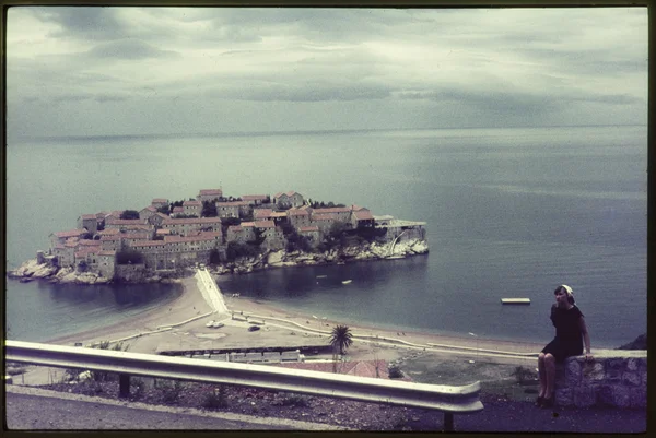 Original vintage colour slide from 1960s, woman sits on a wall by the coast. Royalty Free Stock Images