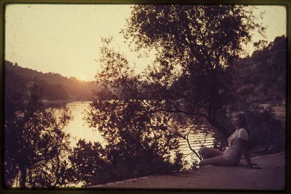 Original Farbrutsche aus den 1960er Jahren, junge Frau genießt Sonnenuntergang am See. Stockfoto