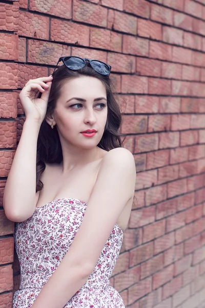 Chica con labios rojos y gafas de sol mira a un lado cerca de la wal de ladrillo —  Fotos de Stock