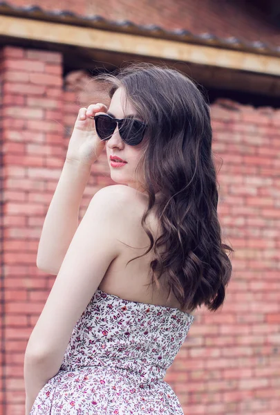 Fille avec des lèvres rouges dans les lunettes de soleil se retourne près de la brique — Photo