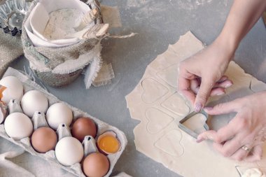 Kadının elleri kalp şeklinde bir teneke kutuyla hamuru kesiyor.