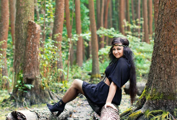 Usmívající se dívka sedící na kládu v zeleném lese — Stock fotografie