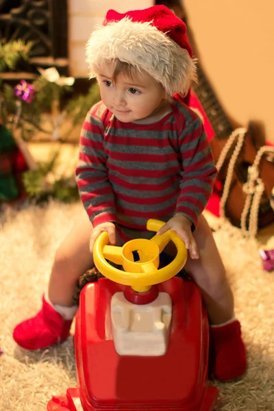 Smiling child in Santa hat is sitting in a baby car — Stock Photo, Image