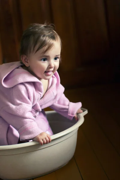 Smiling baby in a bathrobe sits in a basin — Stock Photo, Image