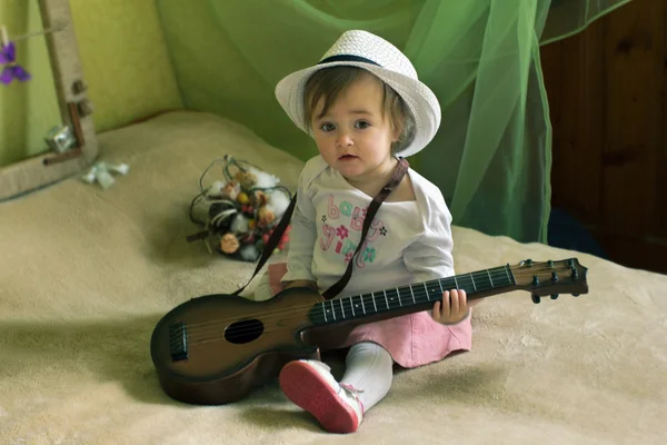 Baby girl with guitar sitting on the bed — Stock Photo, Image