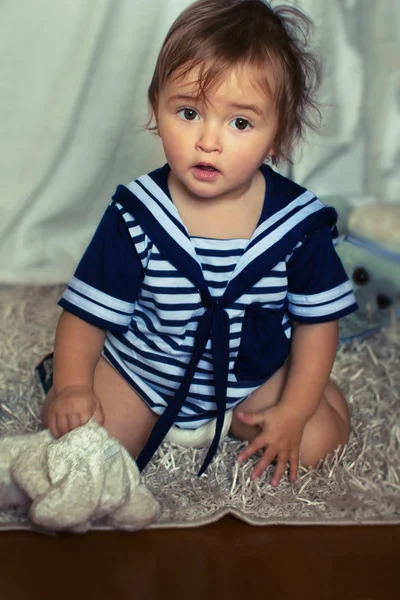 Indignant baby girl in the nautical striped vest sits on the car — Stock Photo, Image