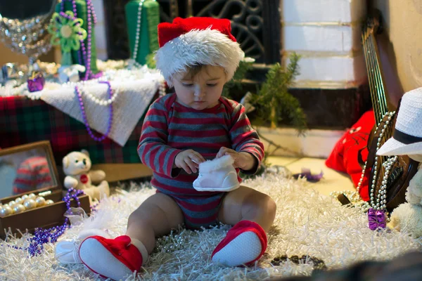 Baby in Santa hat sitting and looking at her shoes — Stock Photo, Image