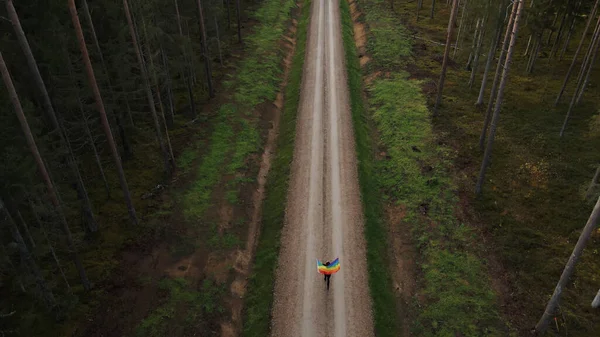 Vista aérea de una mujer corriendo con una gran bandera LGBT arco iris ondeando — Foto de Stock