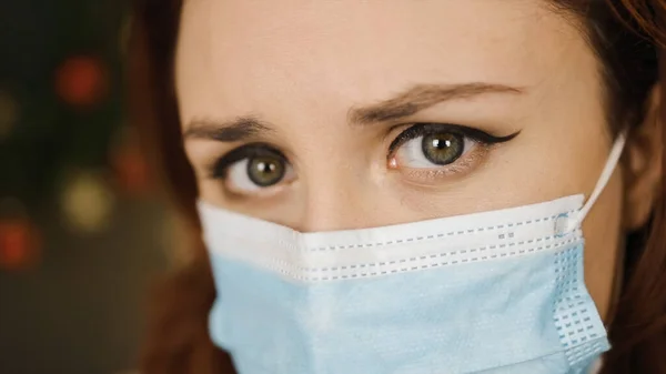 Bardzo bliski widok: Poważna młoda kobieta w masce chirurgicznej patrzy na ciebie — Zdjęcie stockowe