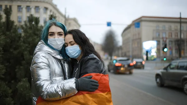 Güzel LGBT kadın çifti kamusal alanda tıbbi maske takarak sarılıyor.