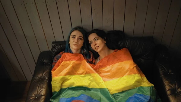 Pareja lesbiana acostada bajo enorme bandera arco iris LGBT —  Fotos de Stock