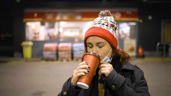 Бідна жінка знижує медичну маску, щоб пити каву в Різдвяному капелюсі — стокове фото
