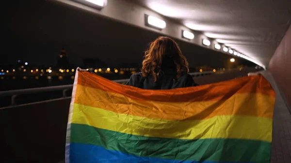 Vista trasera: Mujer LGBT caminando con gran bandera de arco iris —  Fotos de Stock