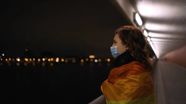 Lesbijki kobieta w medycznej masce uczucie w dół i odwraca się trzymając dużą tęczową flagę — Zdjęcie stockowe