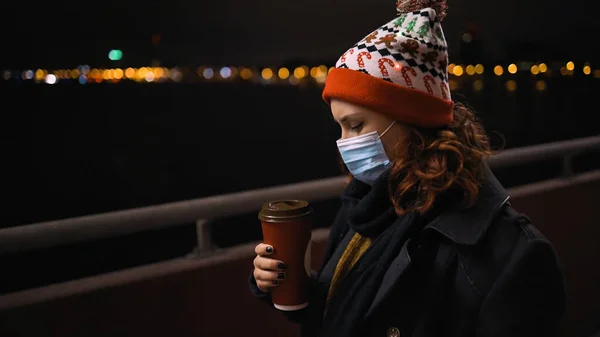 Vista lateral: Mulher cansada em máscara médica e chapéu Xmas detém xícara de café — Fotografia de Stock