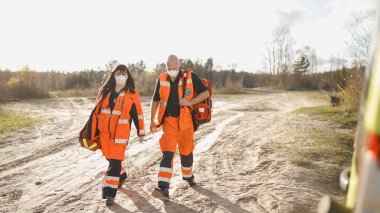 Ambulans aracına doğru yürüyen tam teçhizatlı iki sağlık görevlisi.