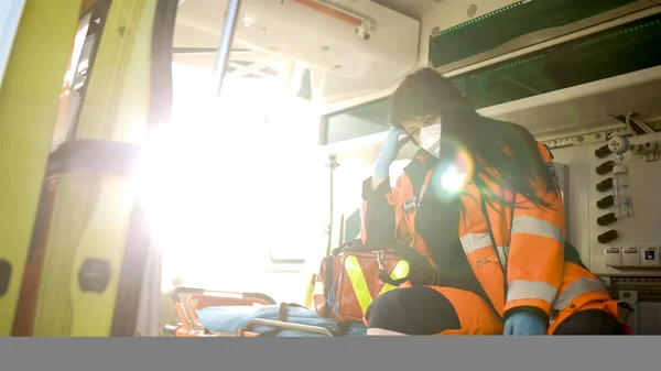 Tired young female emergency doctor sits inside an emergency vehicle looking away — Stock Photo, Image