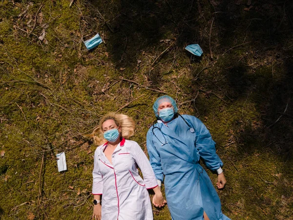 Дві виснажені медики в хірургічних масках, що лежать в лісі — стокове фото