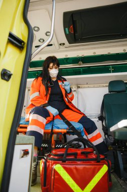 Yüz maskesi takan deneyimli kadın sağlık görevlisi ekipman çantasını kontrol ediyor.