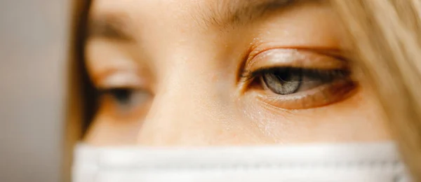 Makro widok oka: Młoda pielęgniarka z niebieskimi oczami nosi maskę medyczną i patrzy w dół — Zdjęcie stockowe