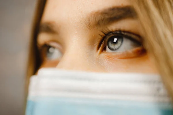 Makró kilátás: Gyönyörű fiatal nő, kék szemekkel, orvosi maszkot visel és félrenéz — Stock Fotó