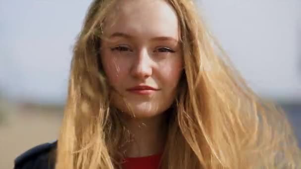 Close view van jonge blonde vrouw kijken naar je in winderig weer — Stockvideo