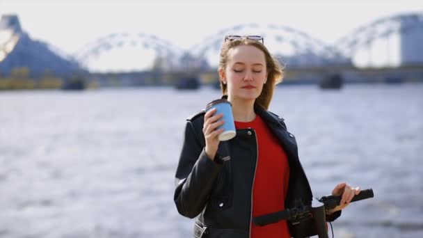 Młoda Europejka stoi w pobliżu białego skutera elektrycznego i pije kawę — Wideo stockowe