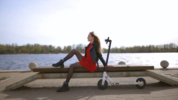 Young blonde woman sits on bench with white electric scooter — Stok video