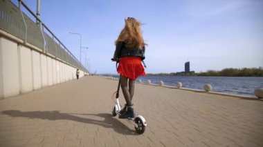 Young blonde woman rides electric scooter. Gimbal follow shot