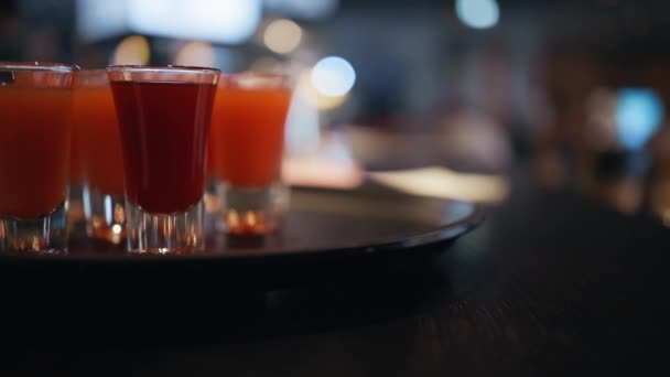 Pan up: Red or orange shots at bar counter in pub with blue blinking light in blurry background — Stock Video