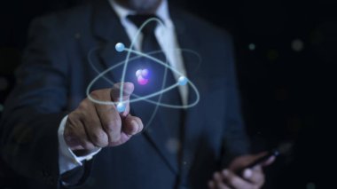 İşadamı mavi arka planda yaratıcı atomu tutuyor. Nükleer füzyon konsepti, sonsuz enerji, ucuz elektrik, gelecekteki teknolojiler. Bilim ve gelecek kavramı
