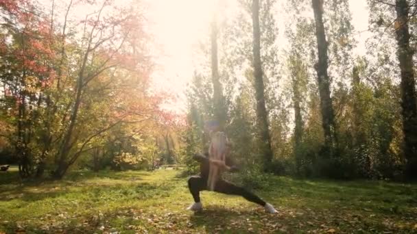Piękna dziewczyna zajmuje się gimnastyką w parku. Sprawność w jesiennym lesie, spokój i uważność, medytacja, elastyczne ciało. koncepcja aktywnego stylu życia. przygotowanie do sezonu na plaży — Wideo stockowe