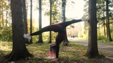 Güzel kız parkta jimnastik yapıyor. Sonbahar ormanlarında sağlık, sakinlik ve farkındalık, meditasyon, esnek vücut. aktif yaşam tarzı konsepti. Plaj sezonuna hazırlanıyorum.