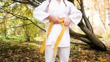 On iki yaşındaki genç bir kız parkta karate yapıyor. Sağlıklı yaşam tarzı kavramı. Spor yapıyor. Dövüş sanatları. Judo, Jiujitsu. Cesur, güçlü. Kimonoya kemer bağlıyor.