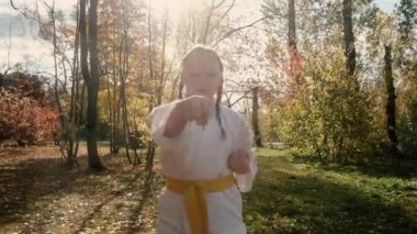 On iki yaşındaki genç bir kız parkta karate yapıyor. Sağlıklı yaşam tarzı kavramı. Spor yapıyor. Dövüş sanatları. Judo, Jiujitsu. Cesur, güçlü. Yumruklarını geliştirir.