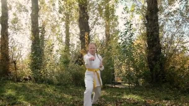 Adolescente de 12 ans est engagée dans le karaté en plein air dans le parc. Concept de mode de vie sain. faire du sport. arts martiaux. Judo, Jiujitsu. courageux, fort. ça donne des coups de poing. séances d'entraînement — Video