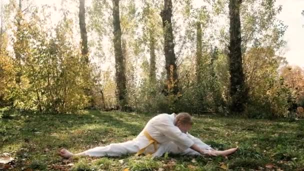 Adolescente 12 años de edad se dedica a karate al aire libre en el parque. Concepto de estilo de vida saludable. practicando deportes. artes marciales. Judo, Jiujitsu. audaz, fuerte. hace un calentamiento. Entrenamientos de torzal — Vídeos de Stock