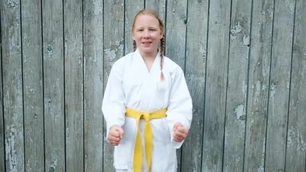 Adolescente ragazza 12 anni è impegnata nel karate sullo sfondo di una recinzione di legno. Un concetto di stile di vita sano. fare sport. arti marziali. Judo, Jiujitsu. pugni coraggiosi, forti e con pugni. Allenamenti — Video Stock