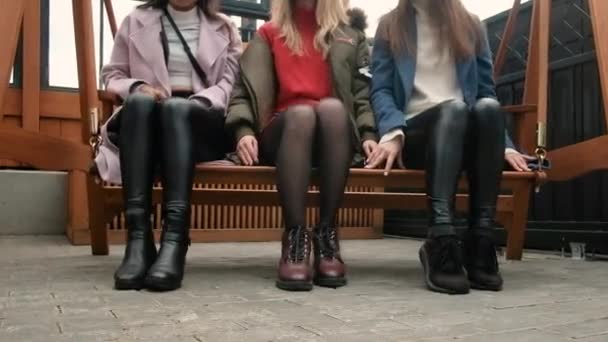 Pernas de meninas fecham. Sorrindo belas amigas juntas na cidade em um banco. As mulheres brincam, divertem-se. Encontro de amigos. comunicação. 25-30 anos.Terraço de verão — Vídeo de Stock