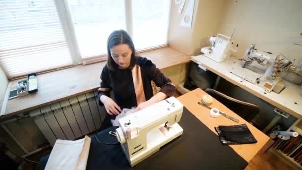 Naaister naait een typemachine aan. Kleding ontwerper. In het proces van werken in de fabriek. Een vrouw op maat maakt modieuze kleding in een werkplaats. Beroep. mode stijl. Uitzicht van bovenaf — Stockvideo