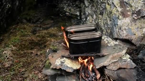 Gotowanie żywności w ogniu w garnku. Obóz w górach.Koncepcja stylu życia podróży. Jedzenie podczas wędrówki. Dwa rondle na kamieniach. Woda się gotuje. herbata, zupa. Węgiel, drewno opałowe. — Wideo stockowe