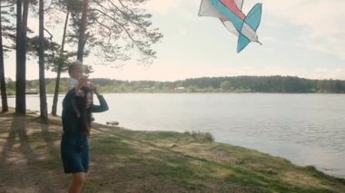 Genç bir anne ve küçük kızı parkta yürüyorlar. Doğada bir çocukla gölün kenarında uçurtma ile oynamak. Aktif yaşam tarzı konsepti. Dikkat et annelik. Dikkat.