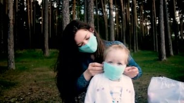 Genç anne, küçük kızına koruyucu bir maske takıyor. Yazın parkta yürüyüş. Koronavirüs salgını. Covid 19. Karantina sırasında aktif yaşam tarzı kavramı. bakım, koruma